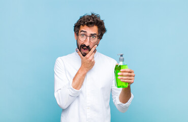young bearded man with mouth and eyes wide open and hand on chin, feeling unpleasantly shocked,...