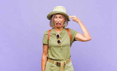 middle age woman looking unhappy and stressed, suicide gesture making gun sign with hand, pointing...