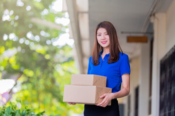 Fototapeta premium Advertising, Business, Transportation, Delivery Concept - The best delivery service. Beautiful Delivery asian woman holding pile of cardboard boxes in front while standing against residential house.