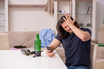 Young unemployed man drinking alcohol at home