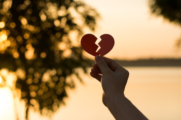 Silhouette broken heart, close up woman hand holding broken heart in the park.
