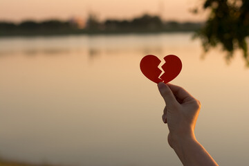 Silhouette broken heart, close up woman hand holding broken heart in the park.
