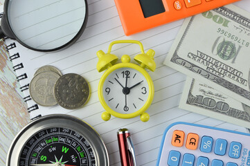 Top view of clock, banknotes, calculators, magnifying glass, coins, compass and pen on the notebook. Business concept. 