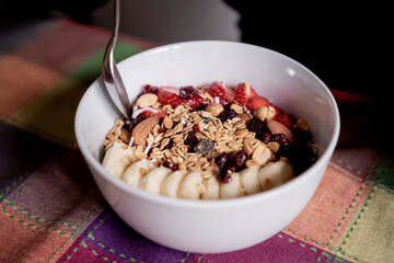 Delicious oatmeal with banana, strawberries, granola, blueberry, coconut and almonds on top with a spoon inside a white plate.