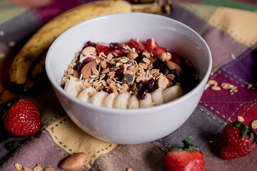 Delicious oatmeal with banana, strawberries, granola, blueberry, coconut and almonds on top, inside a white plate.