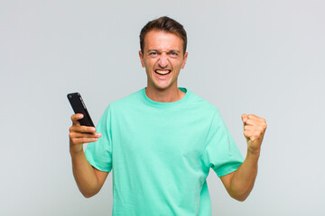 young handsome man shouting aggressively with an angry expression or with fists clenched...