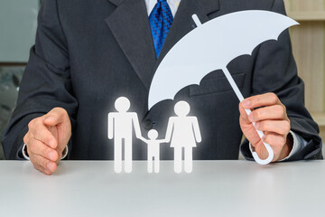 Businessman hold an umbrella and protects or guards family members e.g parents dad, mom and a child