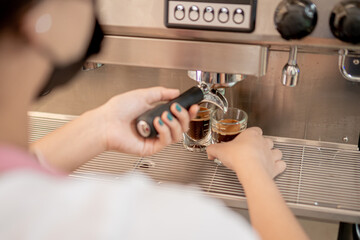 Fototapeta na wymiar Barista serving coffee with a coffee maker in two small glasses