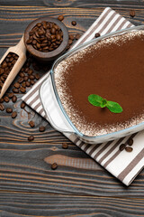 Traditional Italian Tiramisu dessert in glass baking dish and coffee beans on wooden background