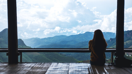 Rear view image of a female traveler sitting and looking at a beautiful mountain and nature view
