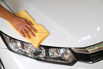 Closeup of white car cleaning  with yellow microfiber cloth by woman's hand.