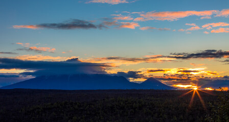 Sunrise from behind the volcano. Volcano peaks in the clouds