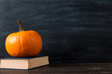 Teacher's table, pumpkin and book, on a chalkboard background. Template concept of autumn mood, halloween and Thanksgiving. Copy space.