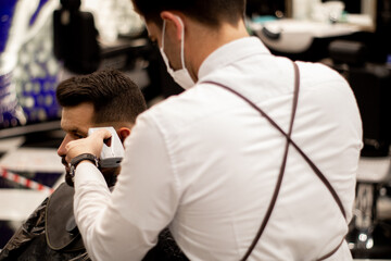 Fototapeta na wymiar Young barber on his back wears a mask while working