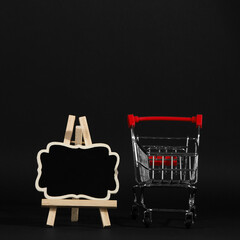 A frame on a stand and shopping cart on a black background, a blank for the design, concept. Copy...