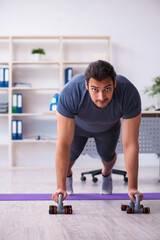 Fototapeta premium Young handsome employee doing sport exercises in the office