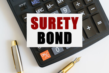 On the table there is a pen, a calculator and a business card on which the text is written - SURETY BOND