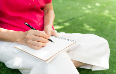 senior retired woman writing diary and sitting in backyard at home