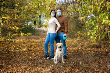 Young couple in medical masks with a dog on a walk