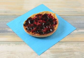 Whole wheat English muffin with black currant jelly preserves on blue napkin on table