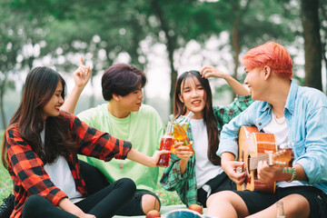 group of happy Asian young people sitting on the guitar and singing in the park