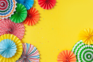 Multicolored paper rosettes of various sizes on a yellow background. Decoration and decor for party, birthday or holiday.