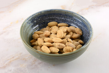 Whole almonds seasoned with Himalayan pink salt in ceramic snack bowl on table