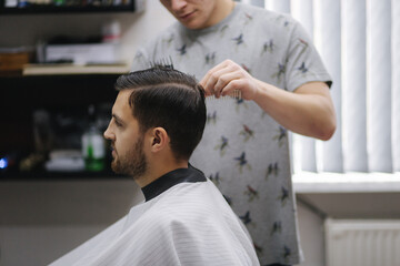 Fototapeta premium Handsome man getting haircut by barber while sitting in chair at barbershop.