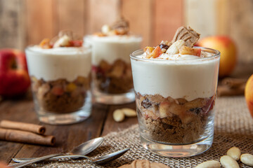 Kuchen im Glas mit Stücken vom Bratapfel, Zimt, Spekulatius, Apfel, Mandeln und Rosinen mit einer Creme aus Quark oder Mascarpone auf einem Tisch aus Holz in einer gemütlichen Küche zu Weihnachten