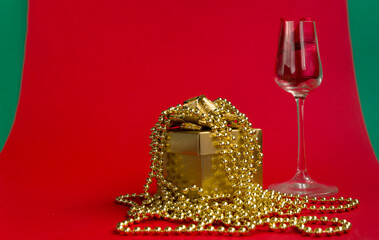 ..Wine glass and gold gift box with beads on a red-green background. The concept of a gift for a girl for a holiday. Close-up Selective focus.