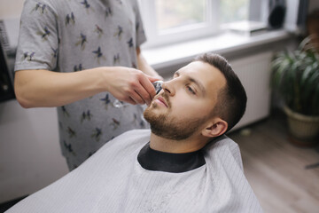 Obraz na płótnie Canvas Professional hairdresser uses a hair clipper for fringing hair for a handsome bearder man. Barbershop