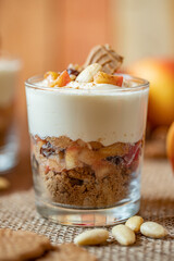 Kuchen im Glas mit Stücken vom Bratapfel, Zimt, Spekulatius, Apfel, Mandeln und Rosinen mit einer Creme aus Quark oder Mascarpone auf einem Tisch aus Holz in einer gemütlichen Küche zu Weihnachten