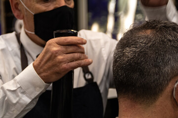 Elderly barber cuts an old man's hair while holding a comb