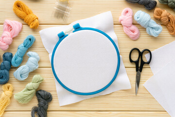 Flat lay of items for embroidery. Hoop, floss threads, needles and canvas on a wooden background