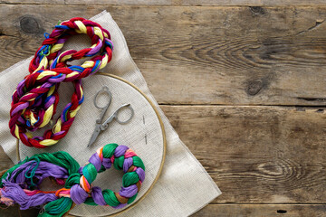 Items for embroidery. Hoop, colorful floss threads and canvas on old wooden background, copyspace