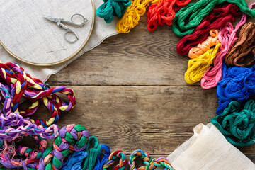 Frame of accessories for embroidery. Hoop, colorful floss threads and canvas on old wooden...