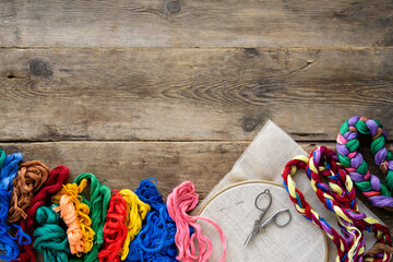 Items for embroidery. Hoop, colorful floss threads and canvas on old wooden background, copyspace