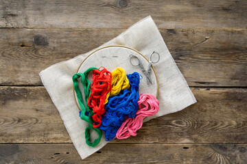 Items for embroidery. Hoop, colorful floss threads and canvas on old wooden background