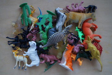 Close-up set of children plastic toy figures: animals and dinosaurs with plants (cacti) on a wooden background. Cold light