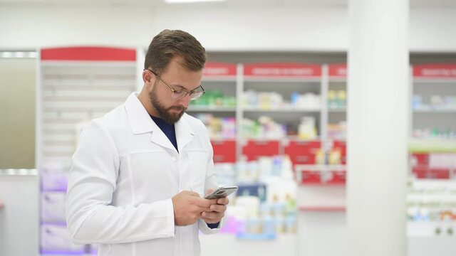 Beautiful male pharmacist doctor in white medical uniform using smartphene.