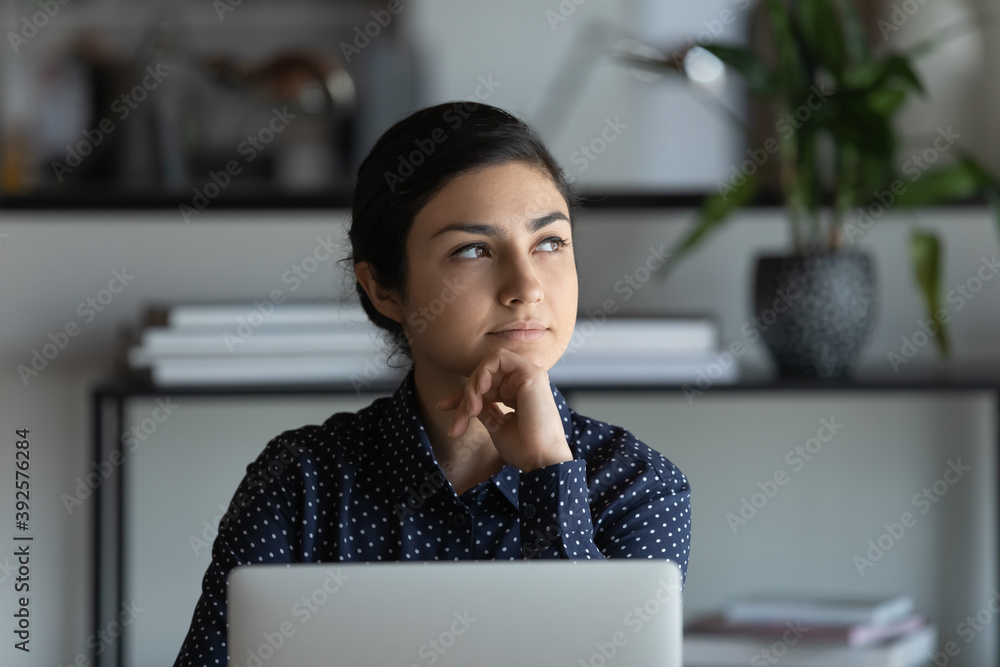 Wall mural close up thoughtful indian businesswoman touching chin, using laptop, sitting at desk in modern offi