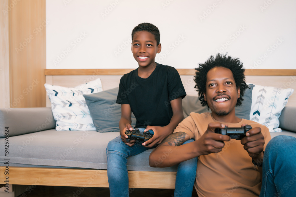 Wall mural father and son playing video games together at home.