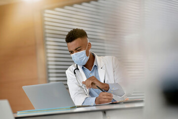 Young doctor working on laptop with face mask