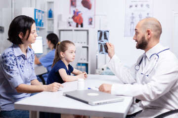 Fototapeta premium Pediatrician examining sick child radiography during medical consultation. Healthcare physician specialist in medicine providing health care services treatment examination.