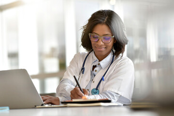 Woman doctor working in office with laptop computer - 392577831