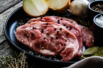 Raw pork chops with onion garlic and seasonings on plate on wooden table