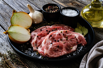 Raw pork chops with onion garlic and seasonings on plate on wooden table