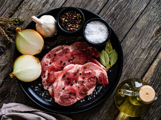 Raw pork chops with onion garlic and seasonings on plate on wooden table
