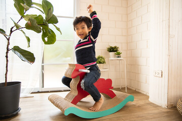 Cute kids playing while parents relaxing at home together, smiling active boy entertaining with paper toy,rocking horse , happy family spending time together in living room on weekend.