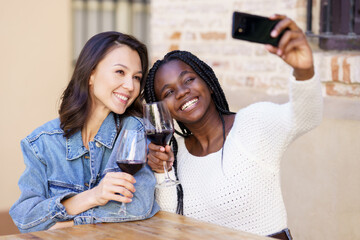 Two women making a selfie with a smartphone while having a glass of wine.